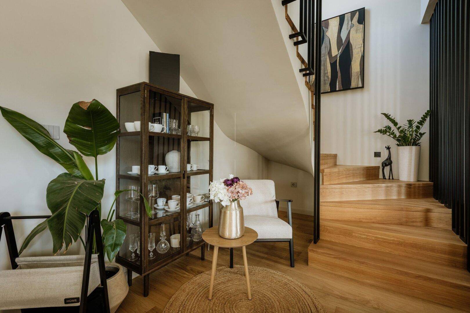 Heller Flurbereich mit eleganter Holztreppe, Pflanzen und modernem Dekor.