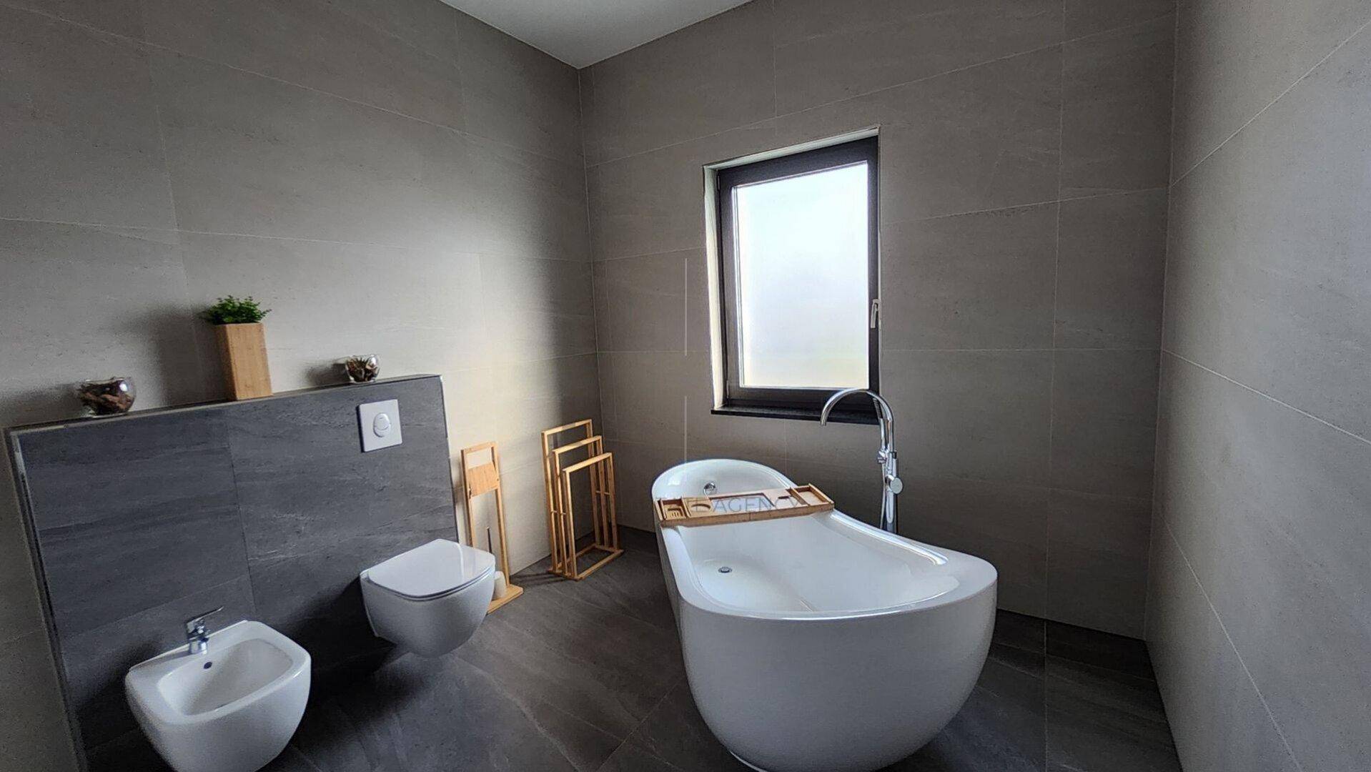 Modernes Badezimmer mit freistehender Badewanne, Bidet und Wand-WC in hellgrauen Fliesen.