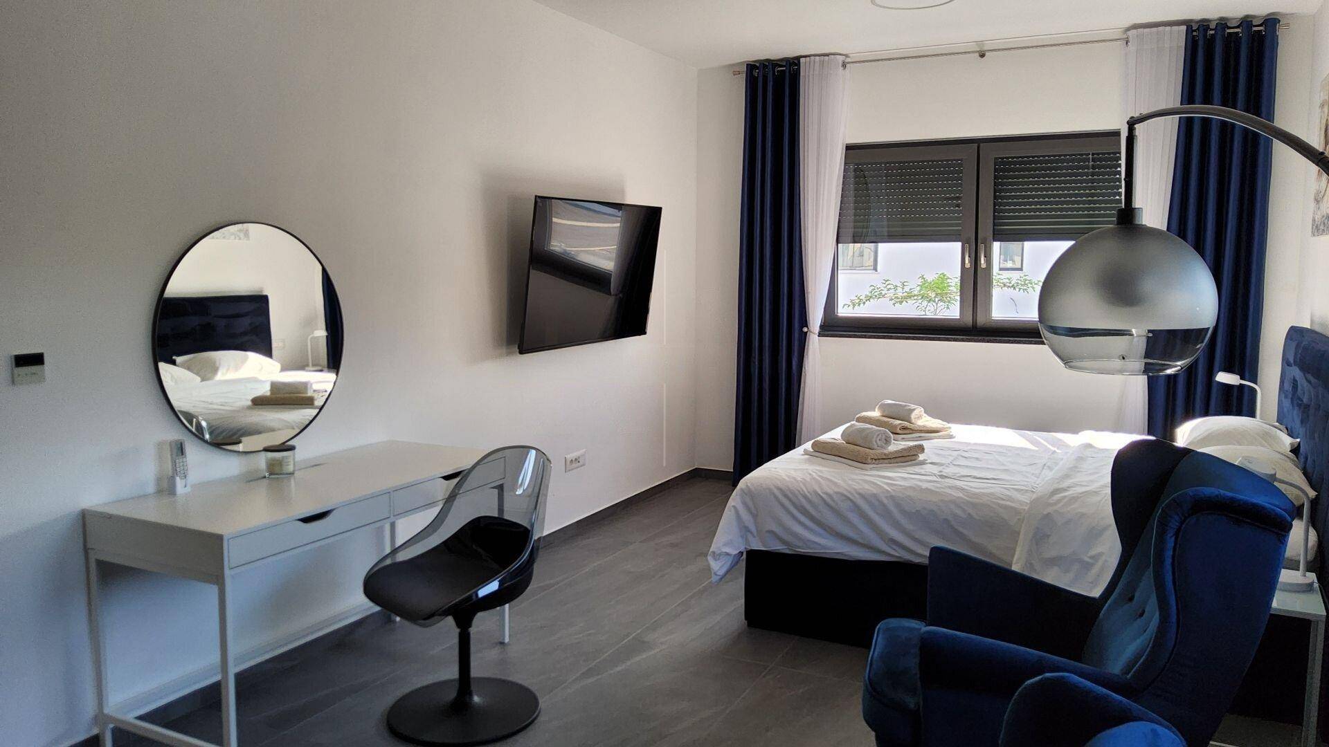 Modern eingerichtetes Schlafzimmer mit Doppelbett, Schreibtisch und Fernseher an der Wand.
