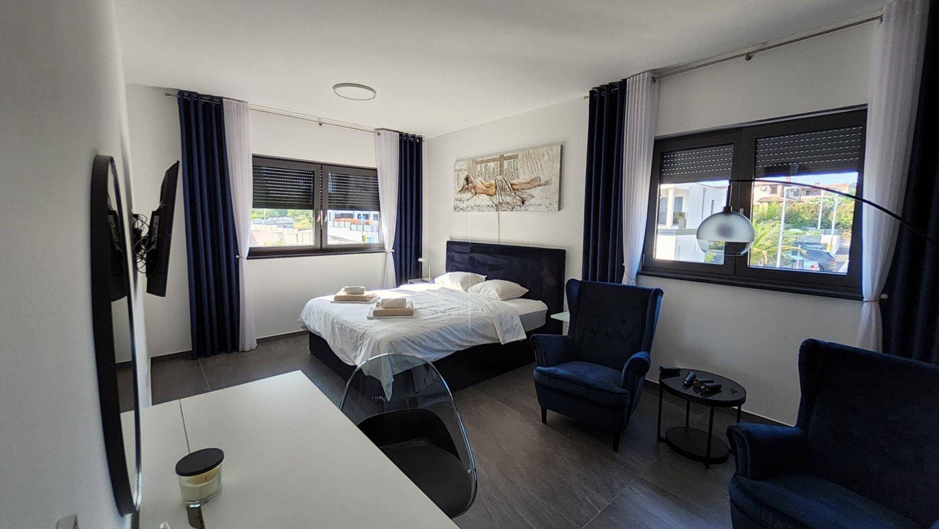 Gemütliches Schlafzimmer mit Doppelbett, blauen Akzenten und großen Fenstern mit Rollläden.