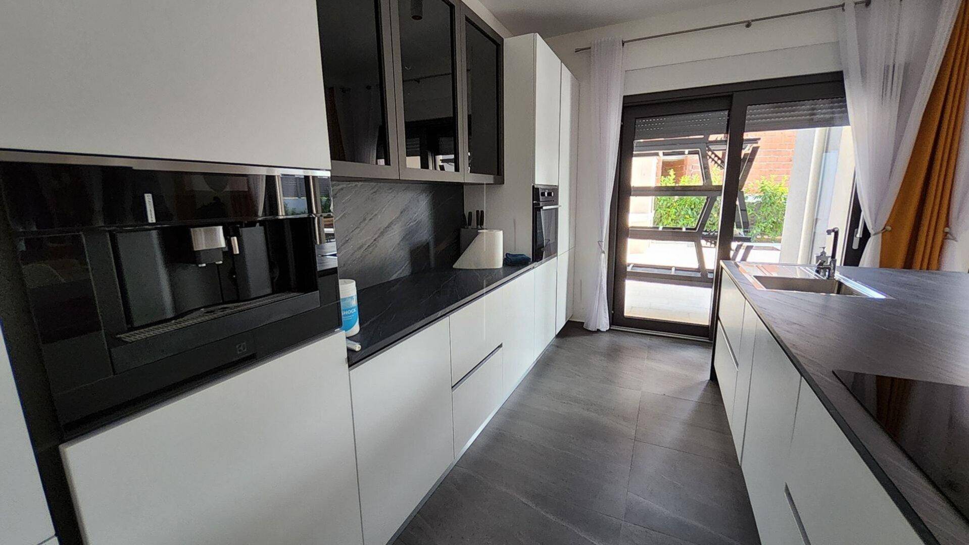 Moderne Einbauküche mit weißen Schränken, dunklen Arbeitsplatten und integrierter Kaffeemaschine.