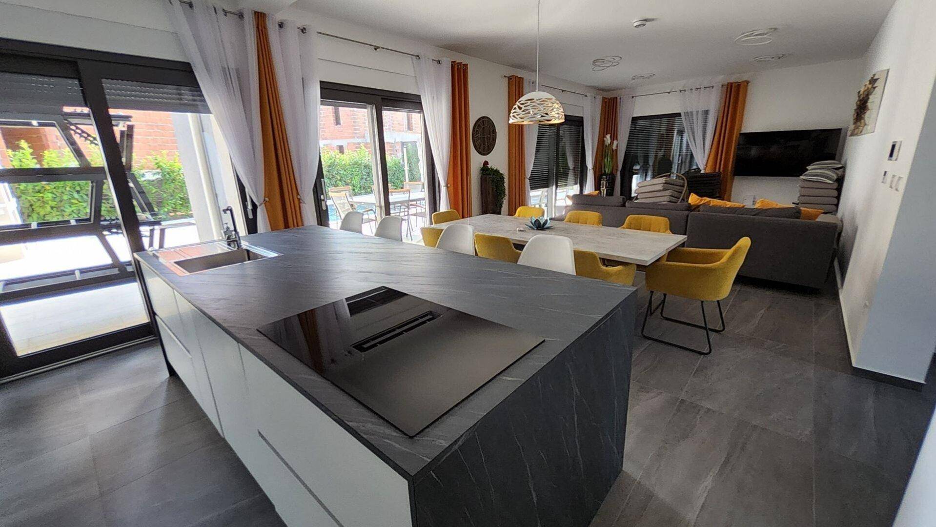 Offener Wohn- und Essbereich mit moderner Küche, großer Kücheninsel und Zugang zur Terrasse.
