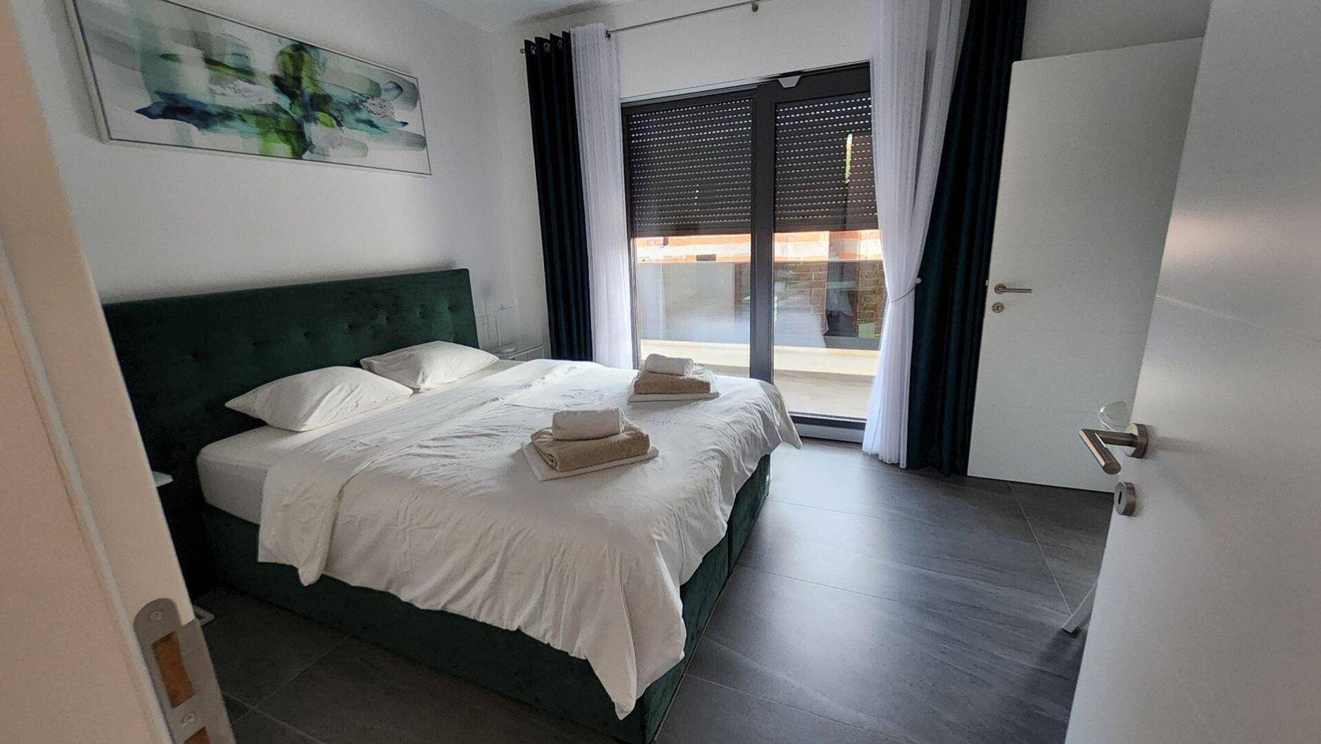 Helles Schlafzimmer mit Doppelbett, Balkonzugang und moderner Einrichtung in ruhigen Farben.