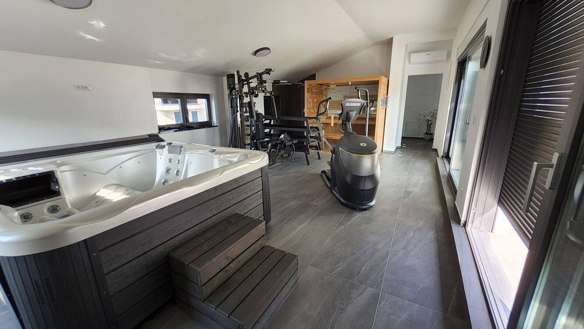 Wellnessbereich mit Whirlpool, Fitnessgeräten und Zugang zu einer großen Dachterrasse.