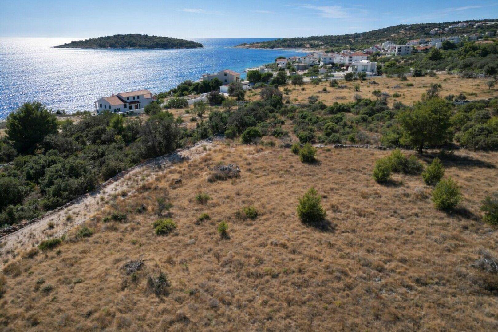 Weitläufiges Grundstück mit trockenem Gras und weitem Blick auf das Meer und die Küste mit Häusern.