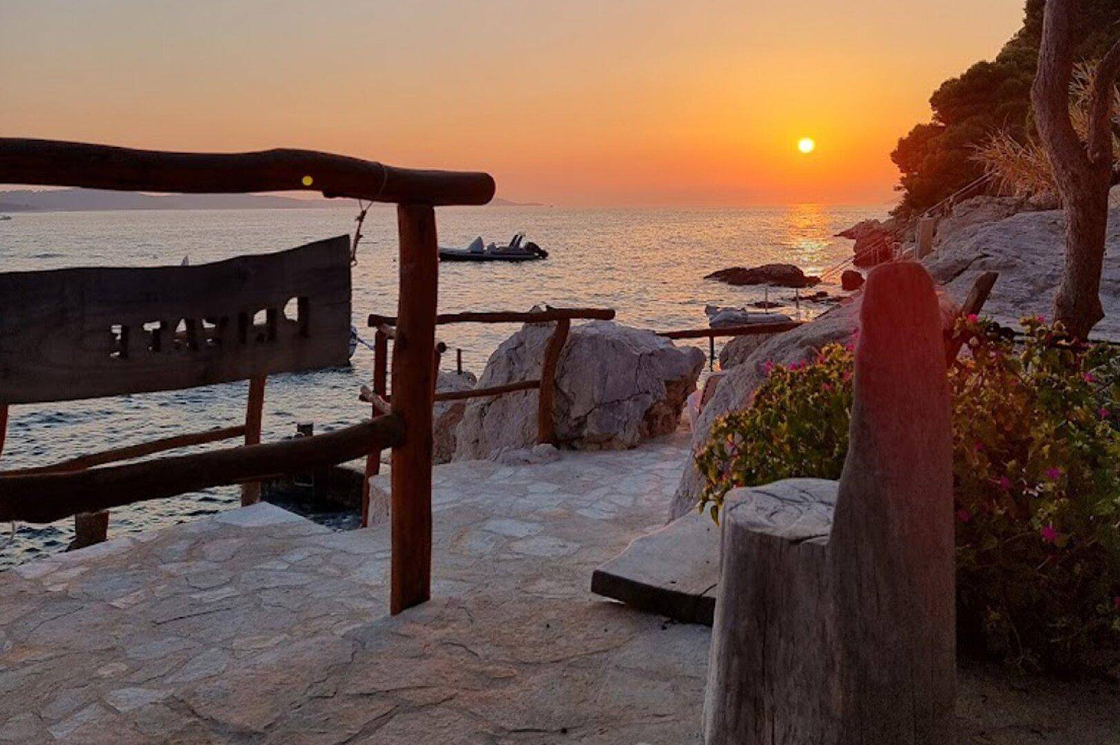 Goldener Sonnenuntergang über dem Meer, beleuchtet einen gepflasterten Bereich mit rustikalem Geländer.