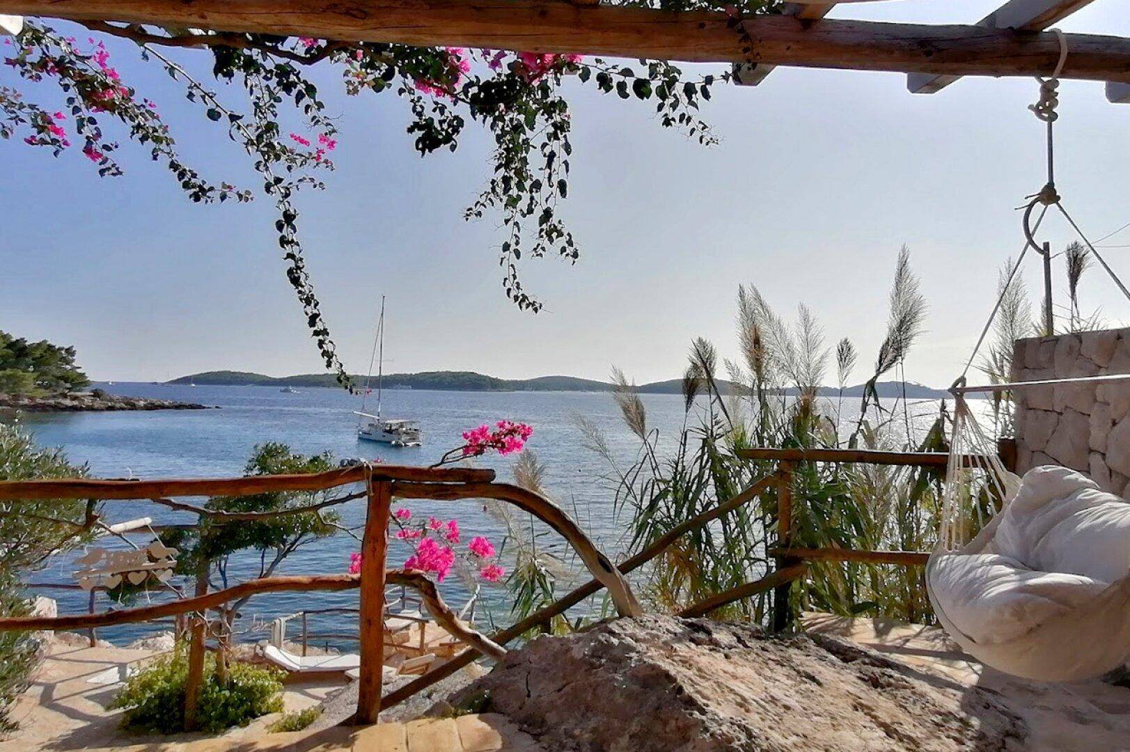 Entspannter Außenbereich mit Hängesessel, umgeben von blühender Bougainvillea und Meerblick.