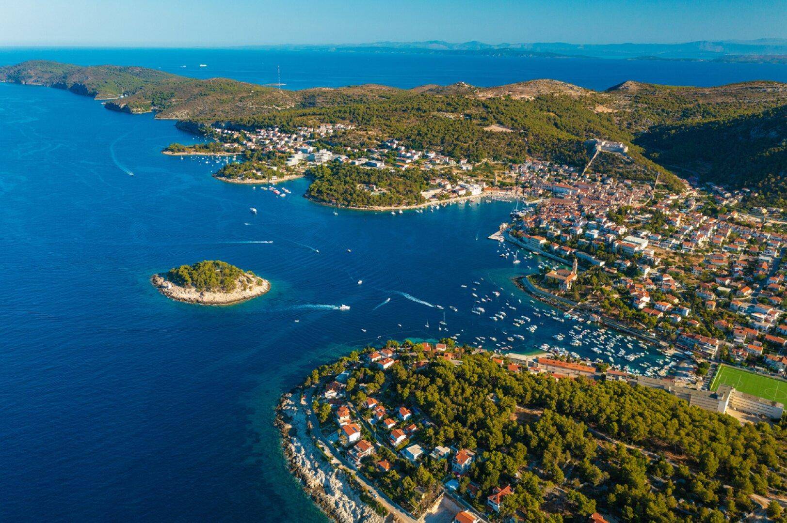Weitläufige Luftaufnahme einer Küstenlandschaft mit einer Stadt, Inseln und zahlreichen Booten im Meer.