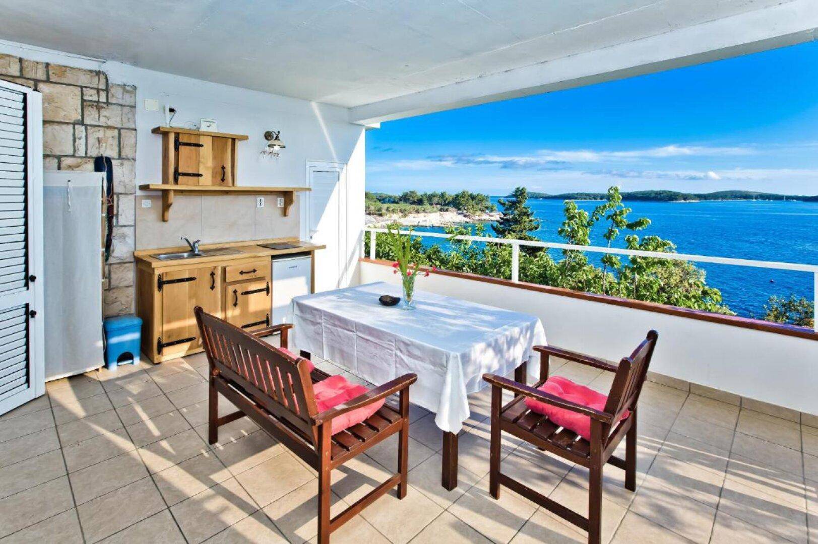 Sonnige Terrasse mit kleiner Küchenzeile und weitem Blick auf das glitzernde Meer.