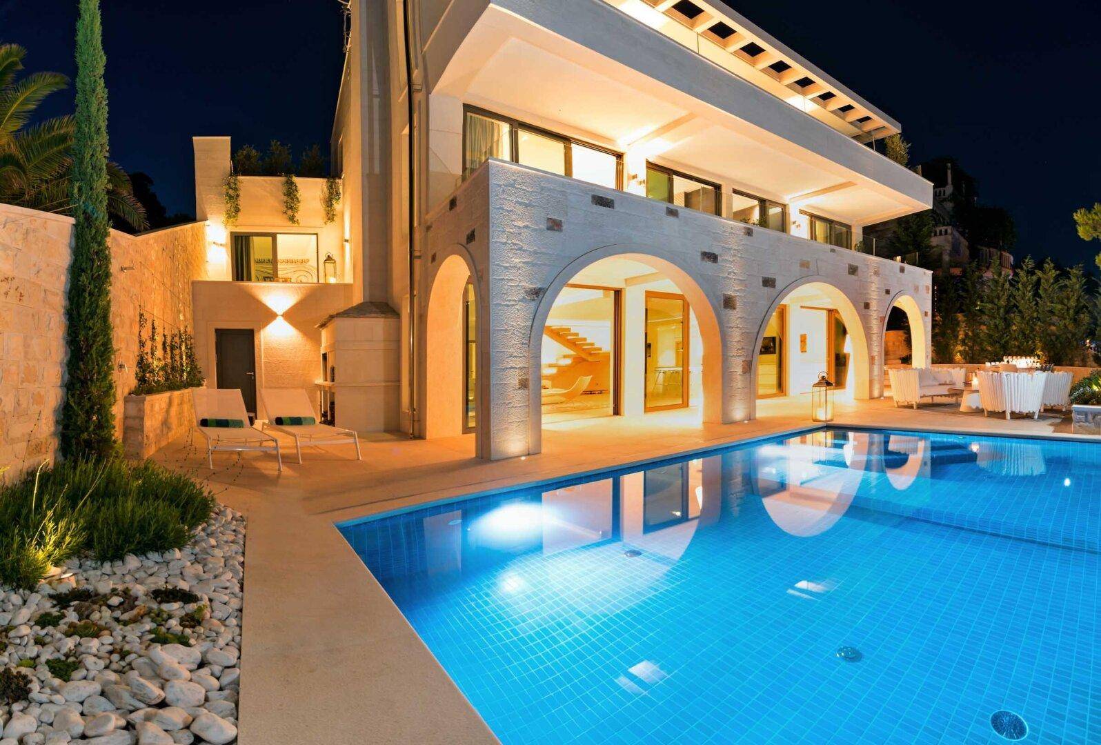 Elegante Villa bei Nacht mit beleuchtetem Pool und stilvollen Lounge-Möbeln auf der Terrasse.