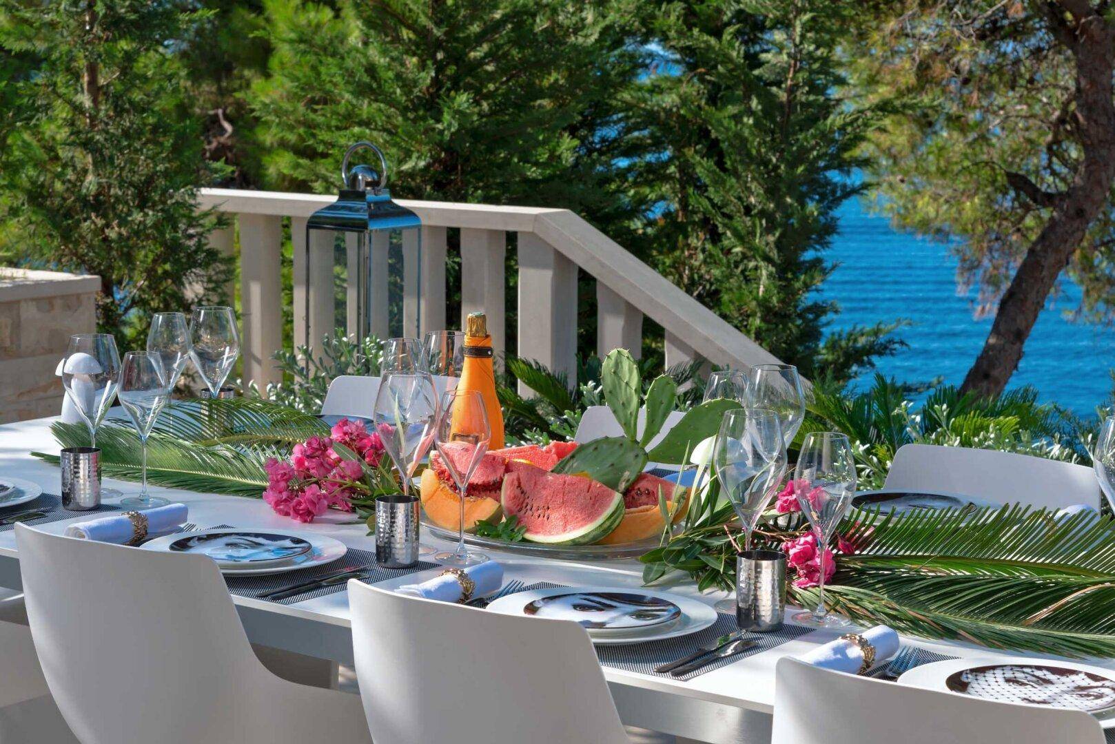 Detailaufnahme eines festlich gedeckten Tisches auf der Terrasse mit atemberaubendem Meerblick im Hintergrund.