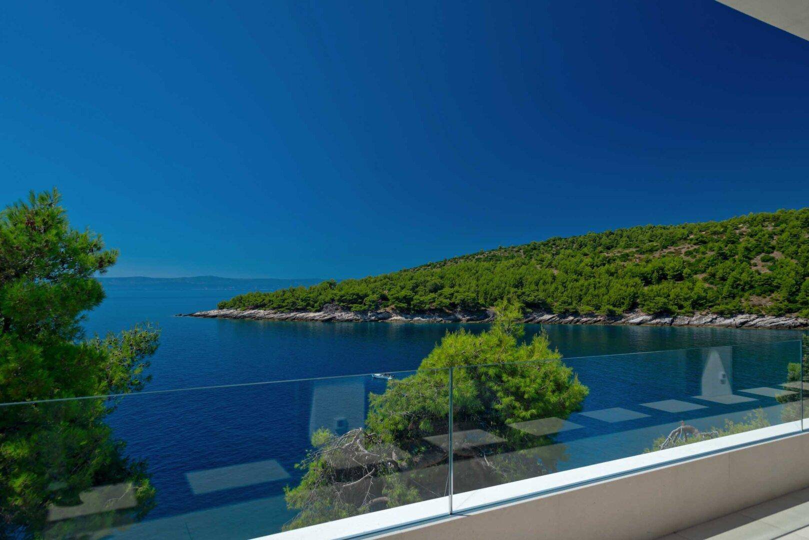 Geräumiger Balkon mit Glasgeländer und atemberaubendem Panoramablick auf das tiefblaue Meer und die Küste.