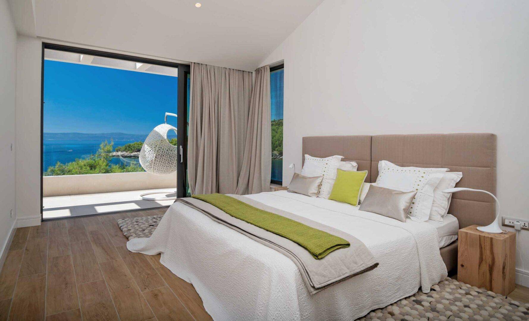 Helles Schlafzimmer mit Holzboden, großem Bett und direktem Zugang zu einem Balkon mit Meerblick.