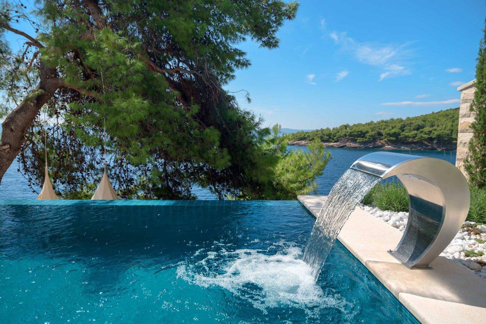 Infinity-Pool mit modernem Wasserfall und weitem Blick auf das Meer und die bewaldete Küste.