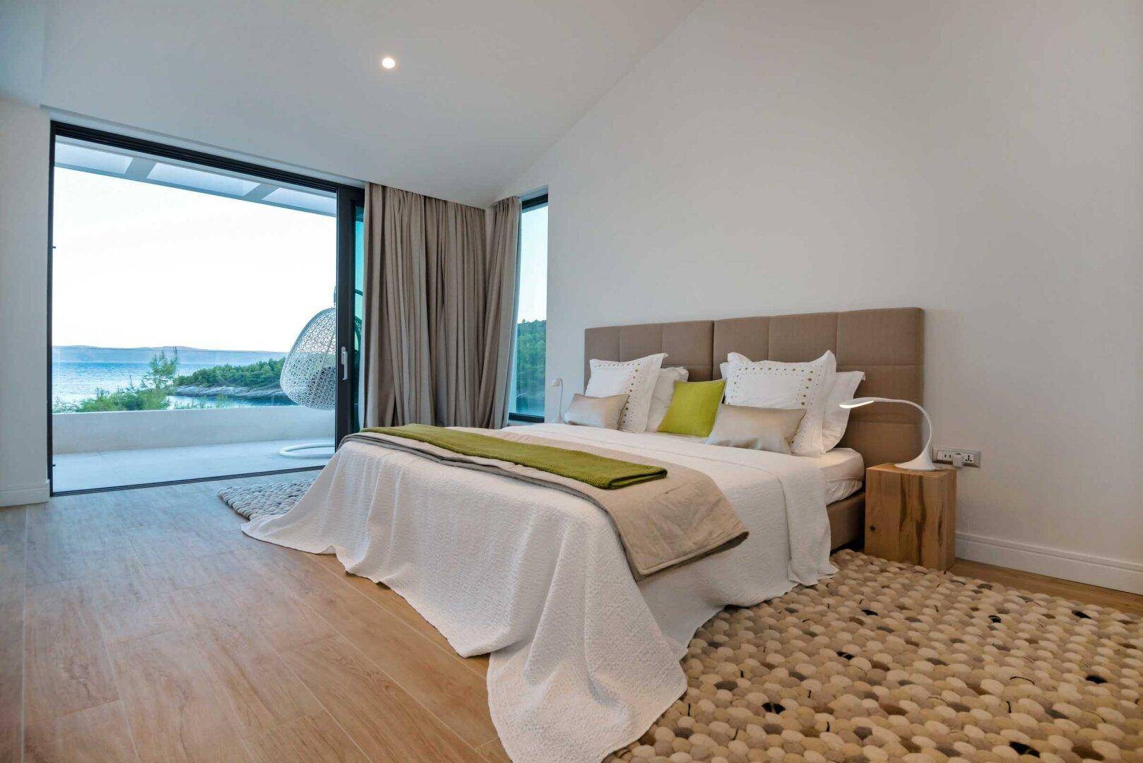 Geräumiges Schlafzimmer mit Holzboden, großem Bett und raumhohen Fenstern, die einen weiten Meerblick bieten.
