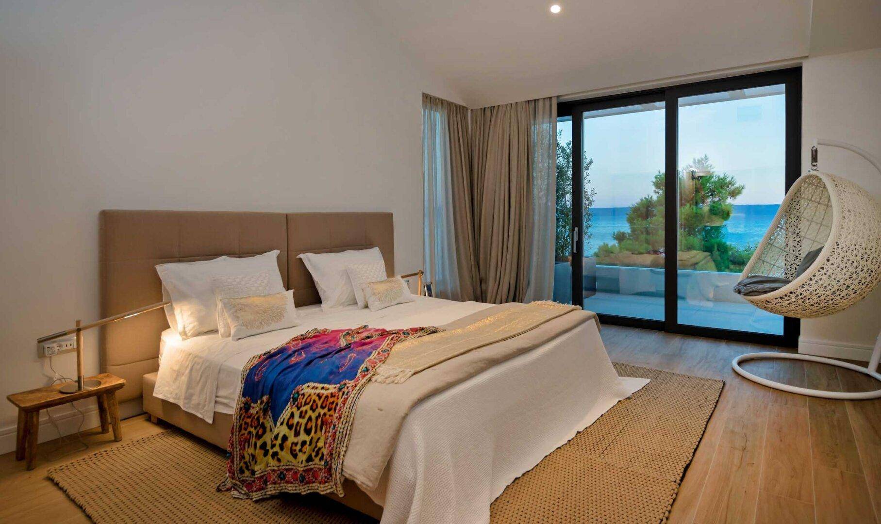 Gemütliches Schlafzimmer mit großem Bett, Holzboden und direktem Zugang zu einem Balkon mit Meerblick.