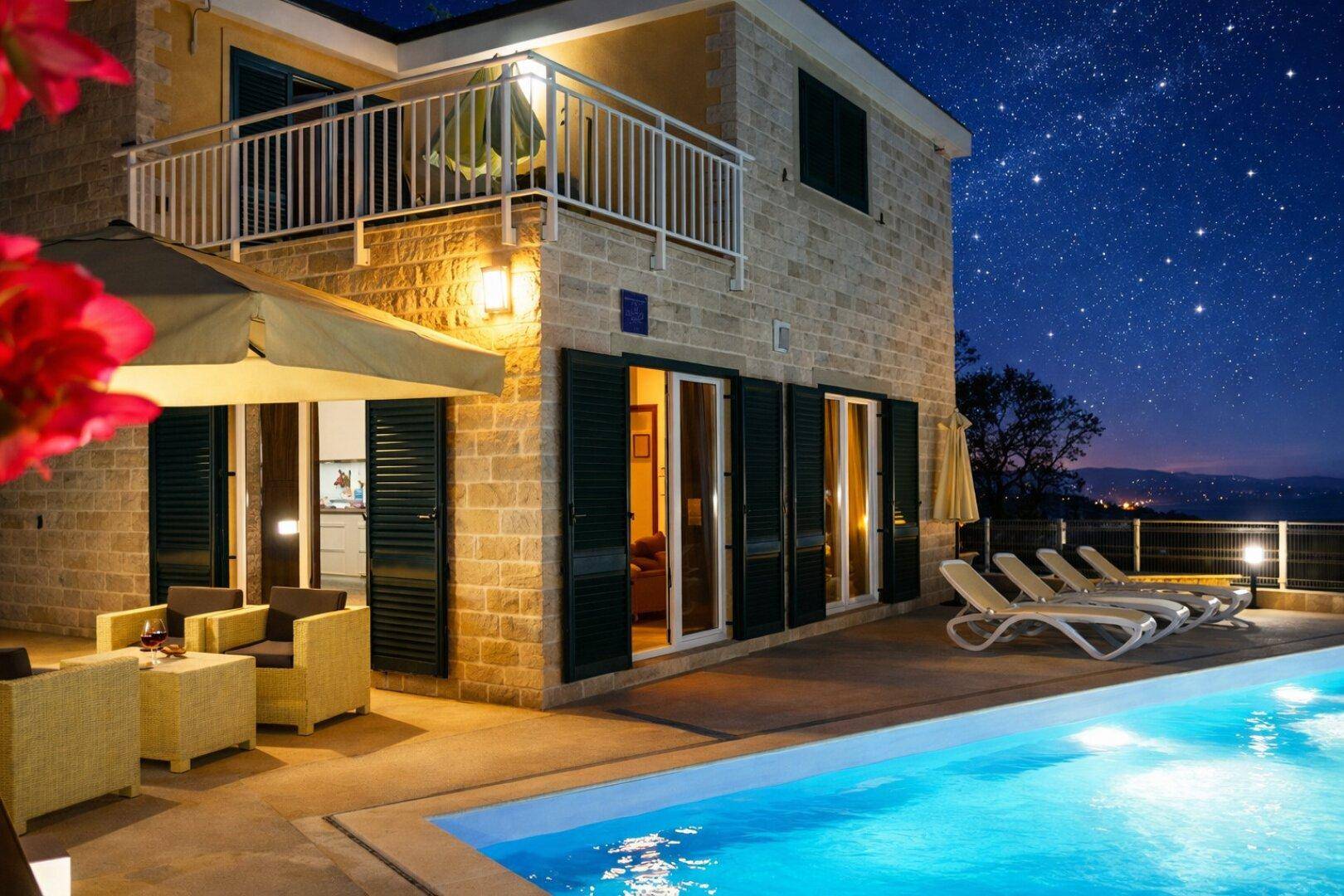 Beleuchteter Poolbereich und Terrasse des Hauses unter einem sternenklaren Nachthimmel.