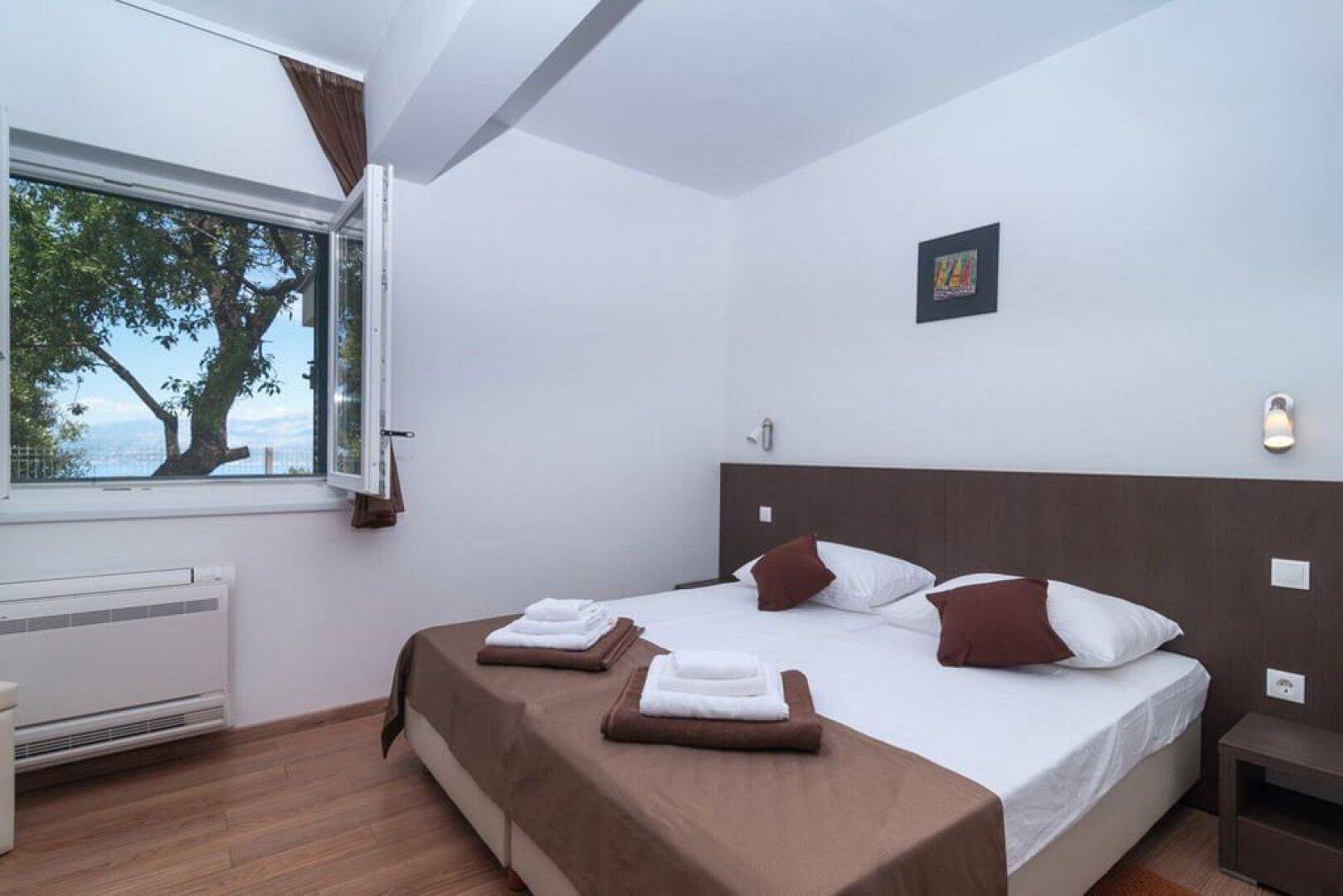 Schlafzimmer mit Doppelbett und Fenster mit Blick auf die umliegenden Bäume.