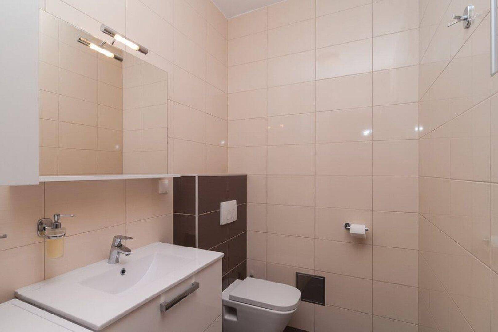 Helles Badezimmer mit Waschbecken, Spiegel und WC, ausgestattet mit modernen Fliesen.