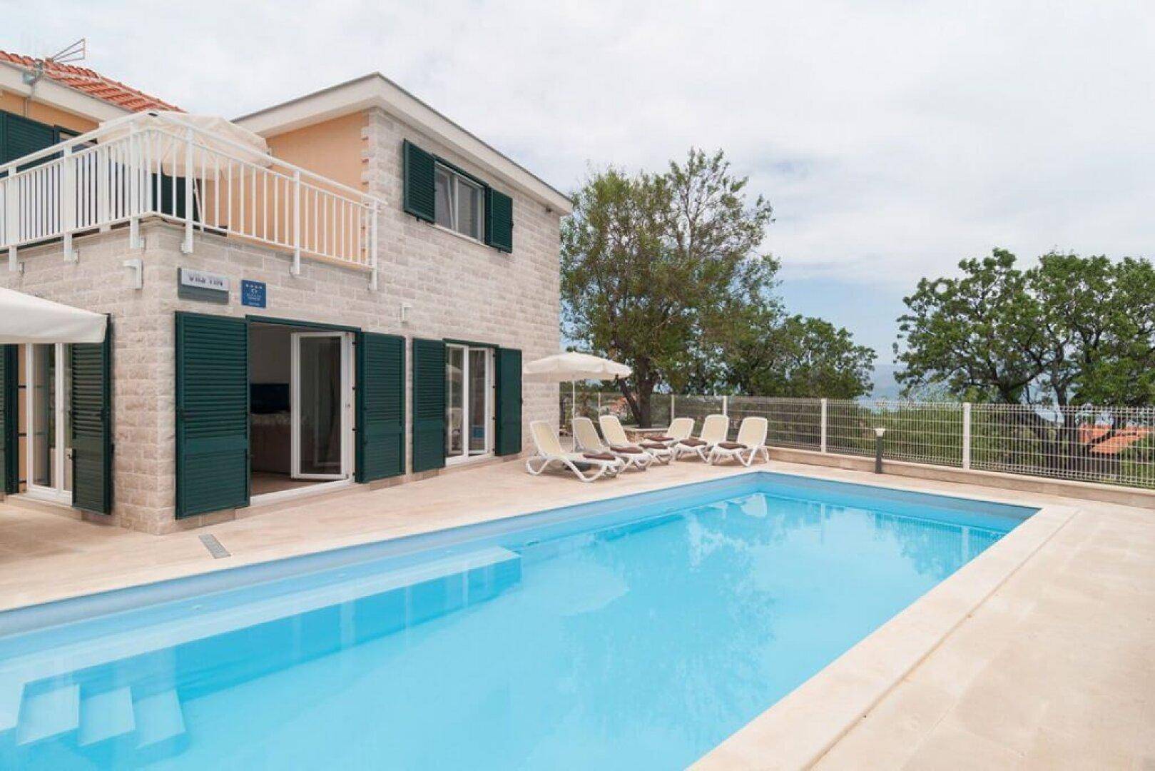 Villa mit großem Pool und Terrasse, umgeben von mediterraner Vegetation und Meerblick.
