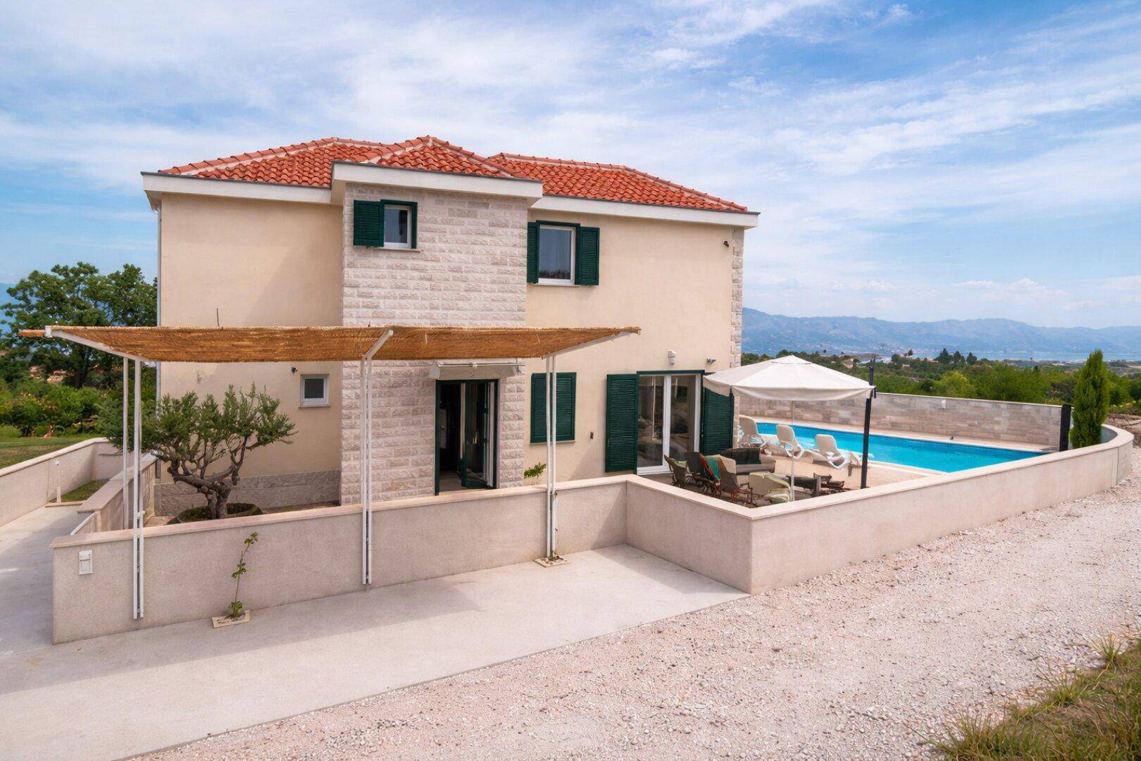 Villa mit Pool, Garten und Carport, umgeben von mediterraner Landschaft und Bergblick.