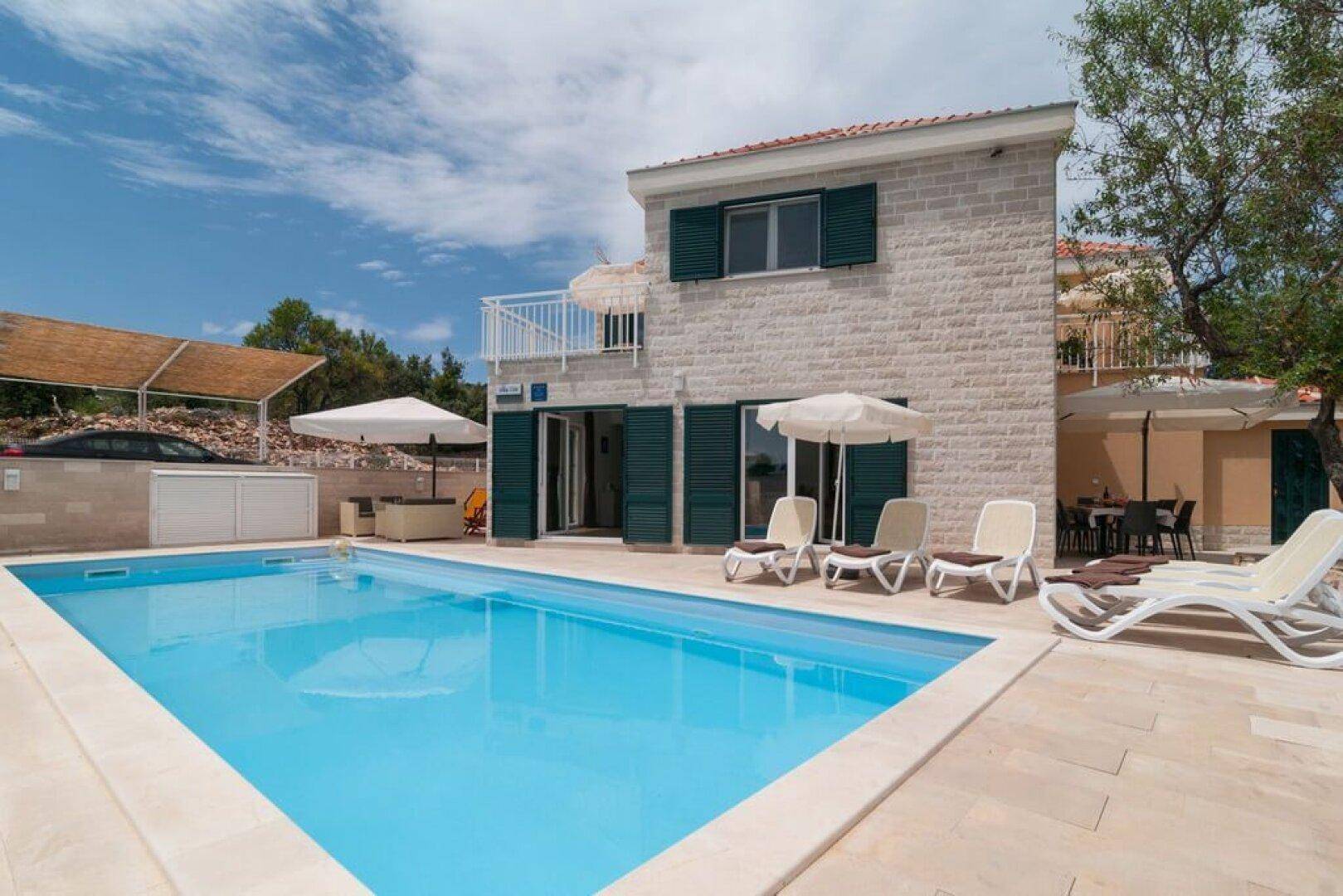 Geräumiger Poolbereich mit Liegestühlen und Sonnenschirmen vor der Villa.