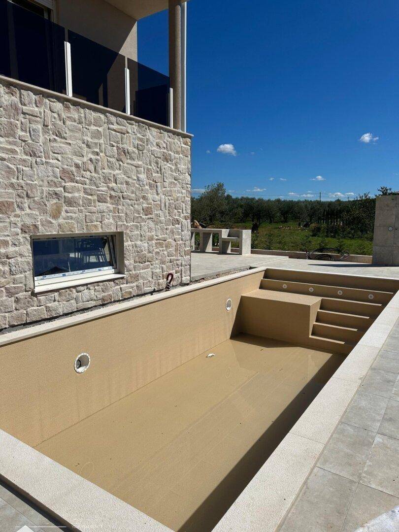Leeres Schwimmbecken mit Stufen und einer steinverkleideten Fassade des Hauses im Hintergrund.