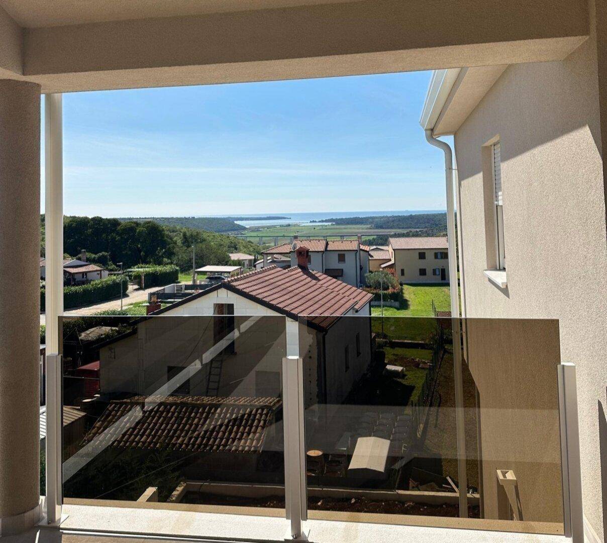 Balkon mit Glasgeländer und weitem Blick über die Dächer der Häuser bis zum Meer in der Ferne.