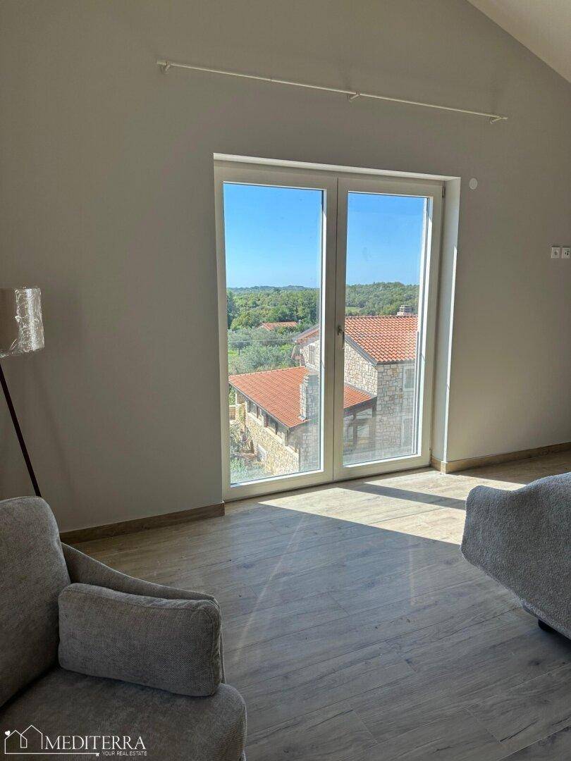 Helles Schlafzimmer mit einer großen Fenstertür, die einen Ausblick auf die umliegenden Häuser bietet.