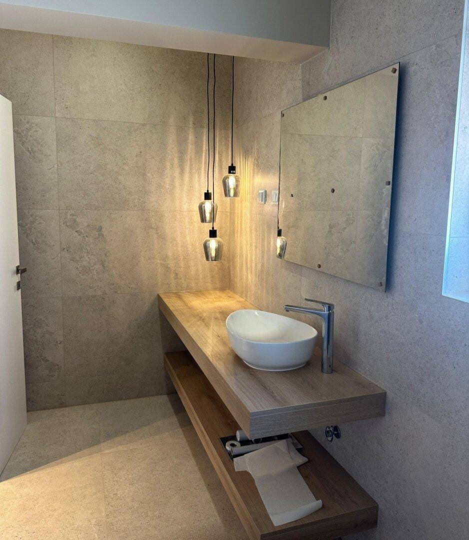 Modernes Badezimmer mit stilvollem Aufsatzwaschbecken auf einer Holzkonsole und eleganten Pendelleuchten.