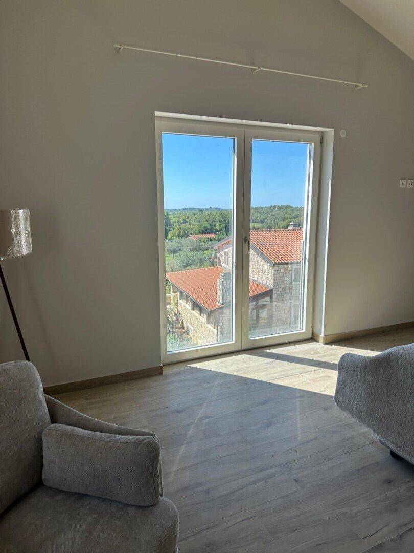 Helles Schlafzimmer mit einer großen Fenstertür, die einen Ausblick auf die umliegenden Häuser bietet.