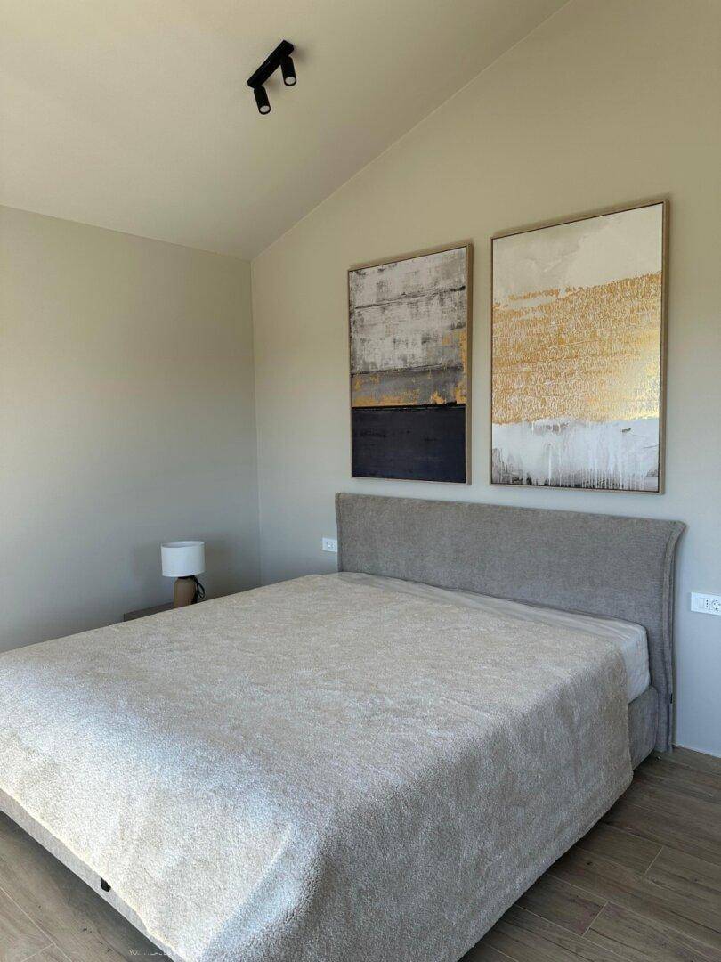 Modernes Schlafzimmer mit bequemem Bett, abstrakten Kunstwerken und hohen Decken, die ein geräumiges Gefühl vermitteln.