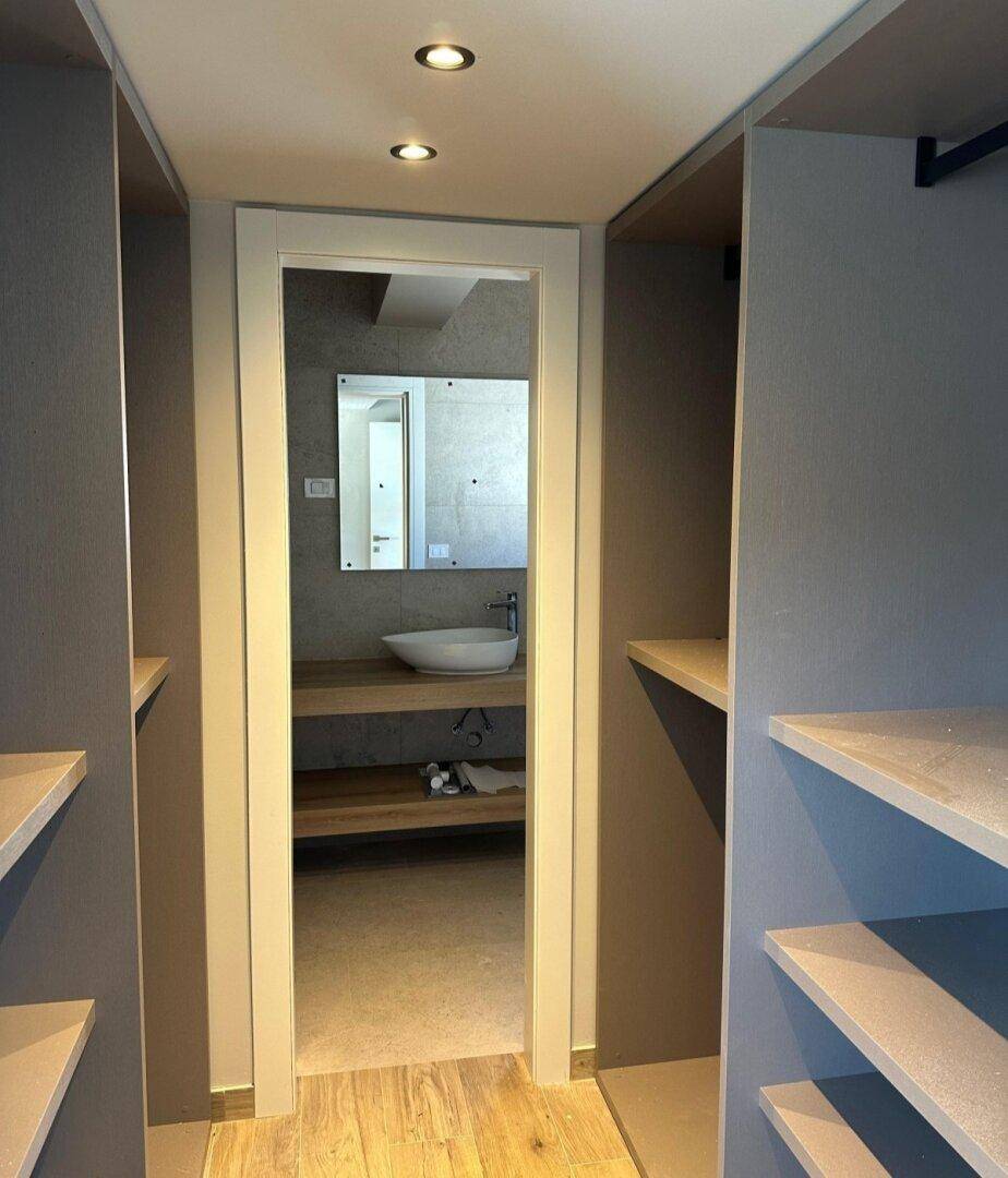 Begehbarer Kleiderschrank mit offenen Regalen und direktem Zugang zu einem modernen Badezimmer.