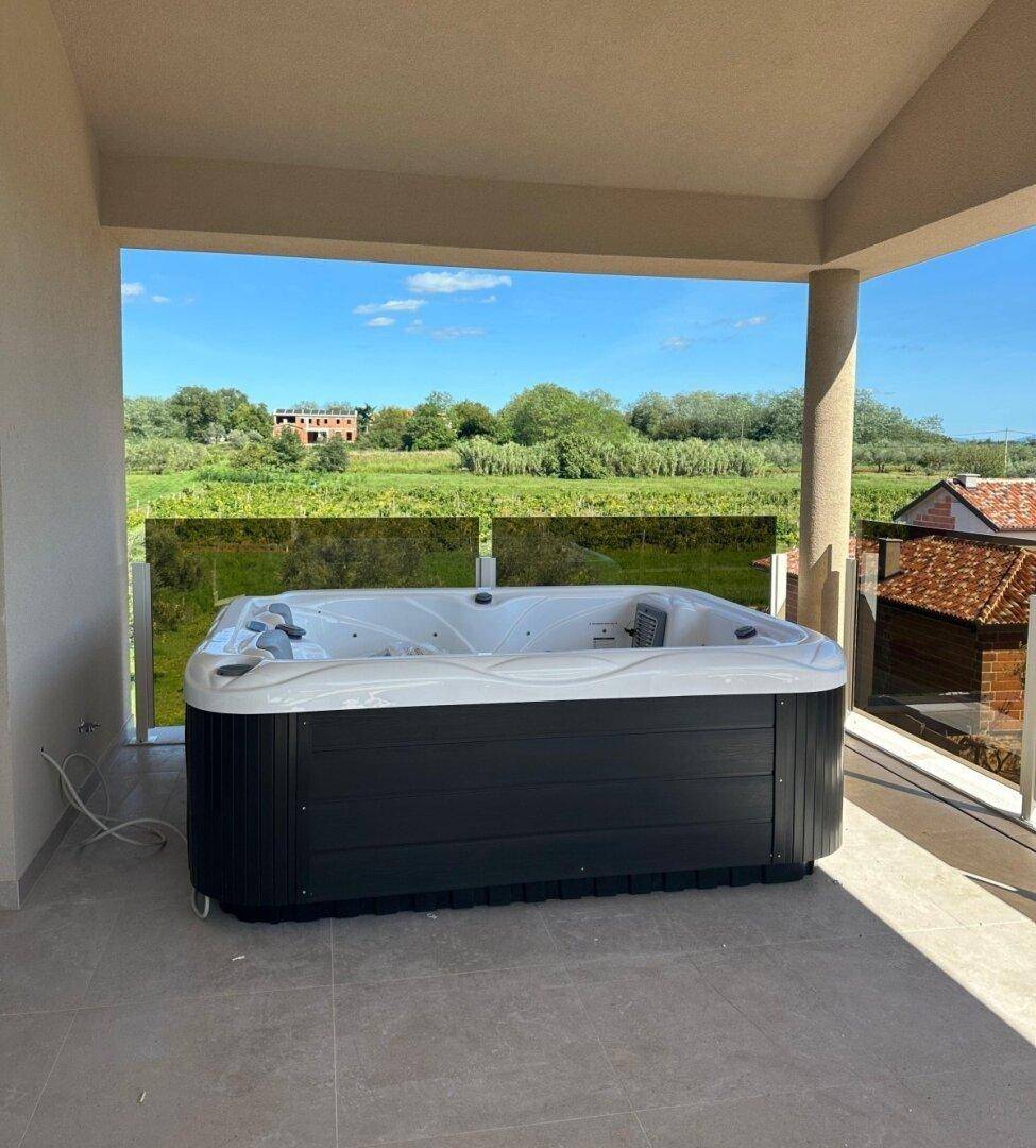 Überdachte Terrasse mit einem Whirlpool und Blick auf die grüne Landschaft und die Umgebung.