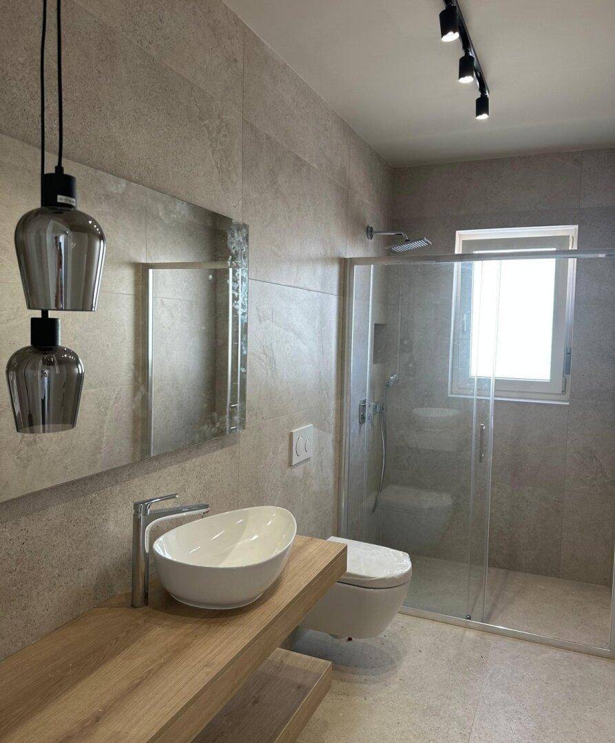 Modernes Badezimmer mit einer begehbaren Dusche, Aufsatzwaschbecken und großformatigen Fliesen.