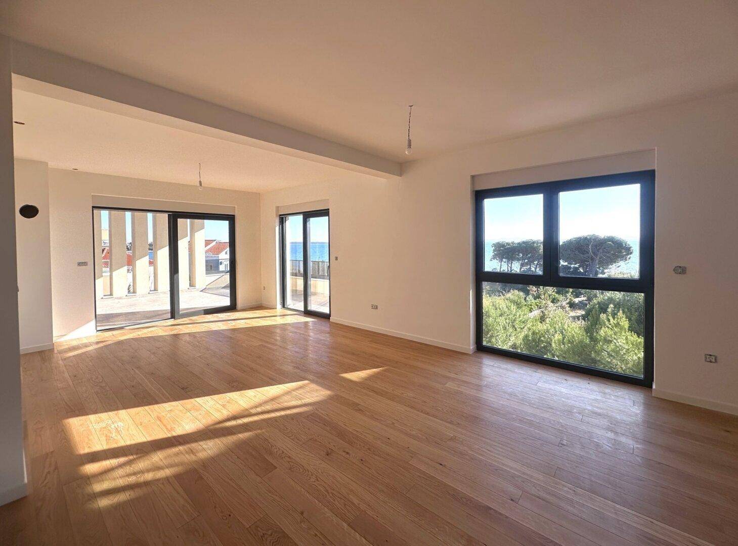 Geräumiges Wohnzimmer mit hellem Parkettboden und großen Fenstern mit Meerblick.