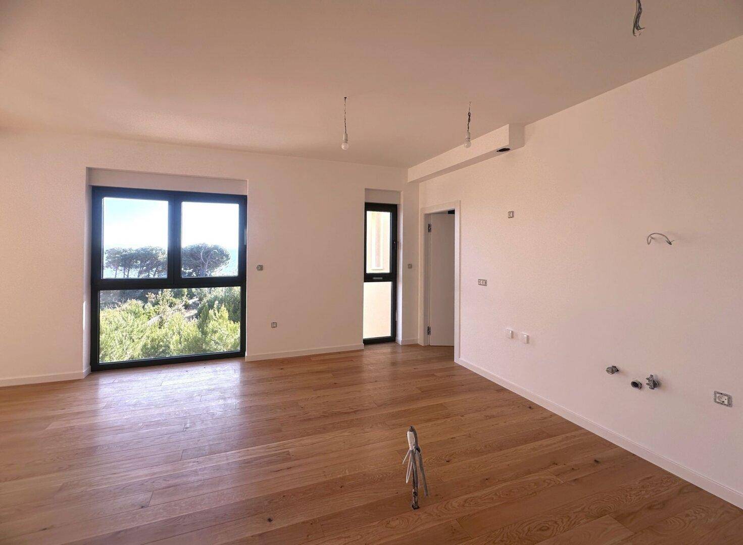 Helles Wohnzimmer mit Holzboden und Zugang zu einem weiteren Raum.