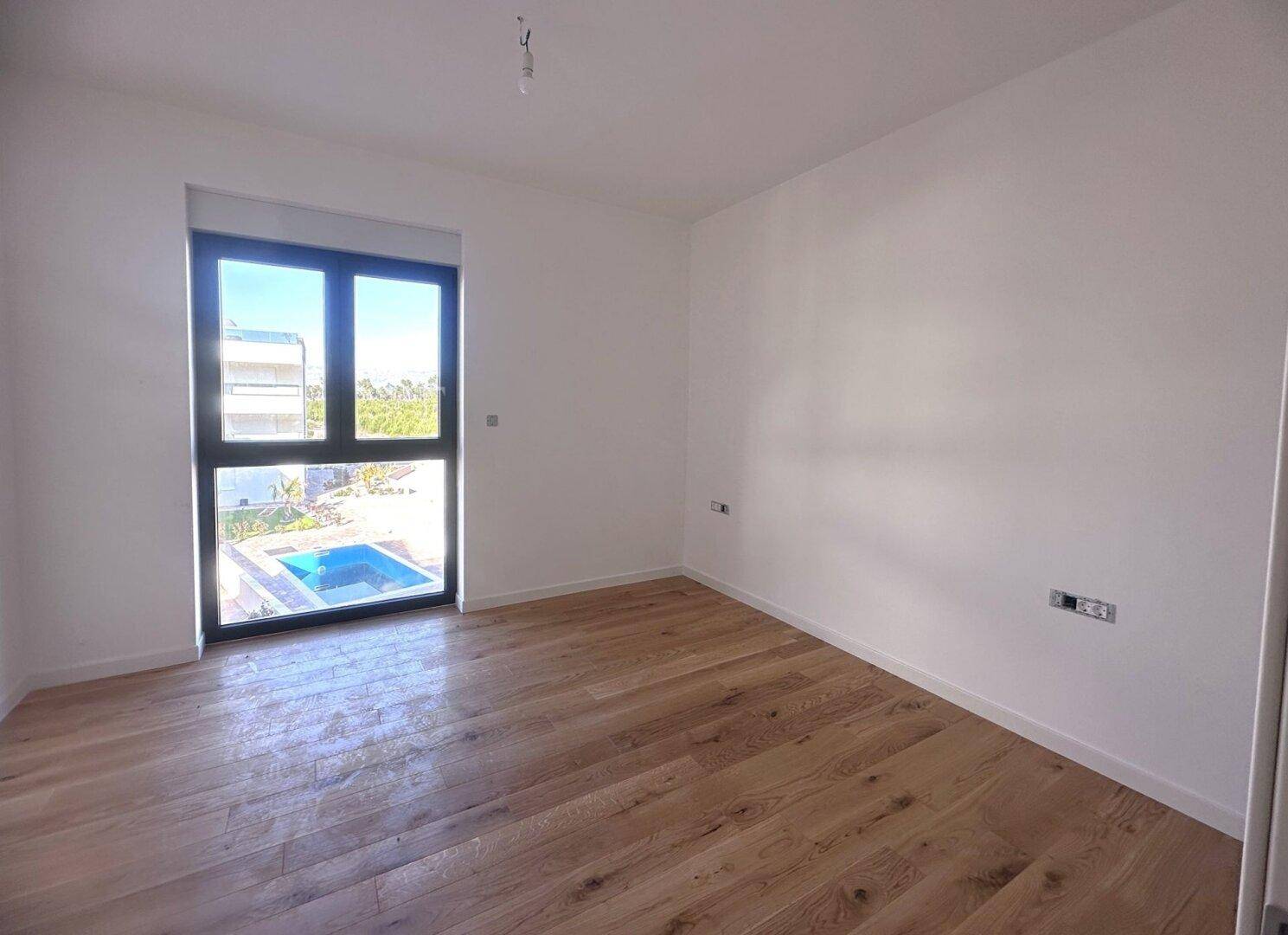 Schlafzimmer mit Holzboden und Fenster mit Blick auf den Poolbereich.