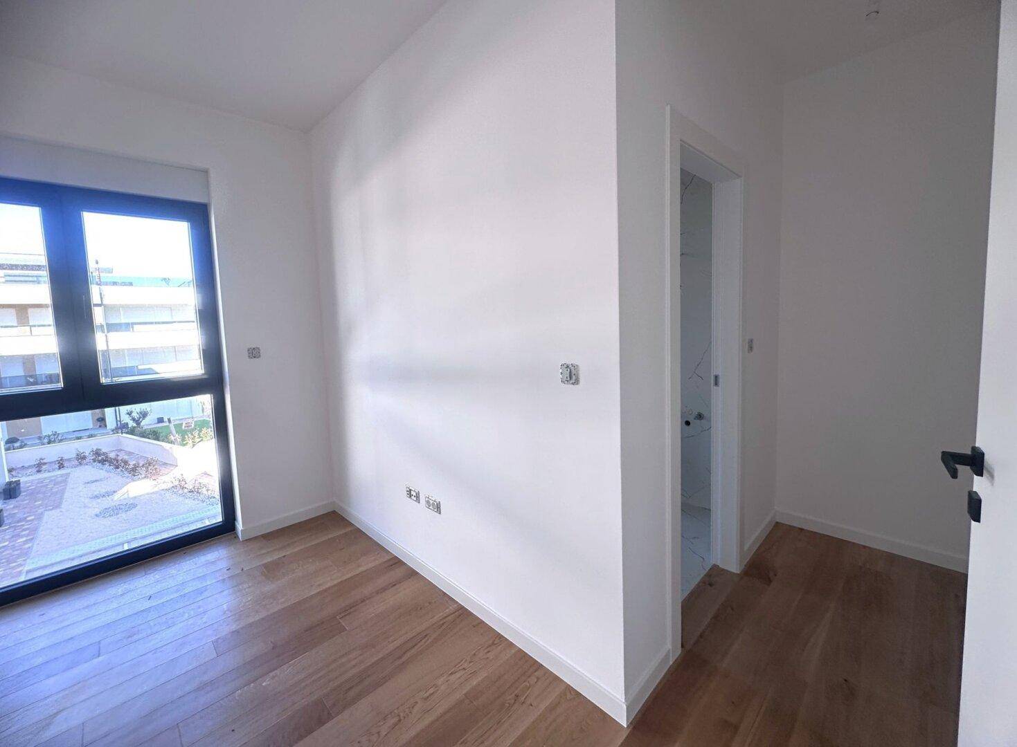 Helles Schlafzimmer mit Holzboden und Zugang zu einem modernen Badezimmer.