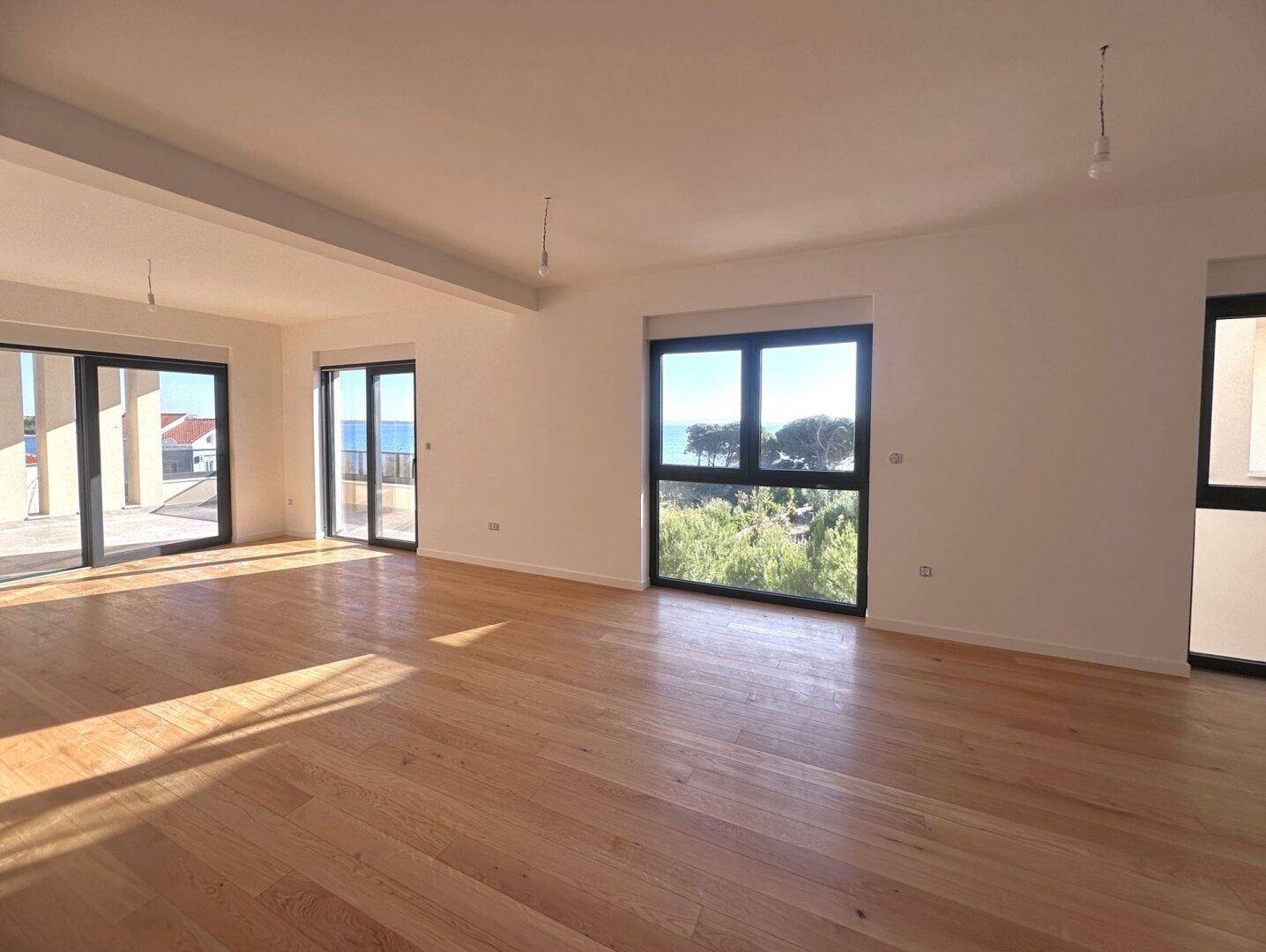 Geräumiges Wohnzimmer mit hellem Parkettboden und großen Fenstern mit Meerblick.