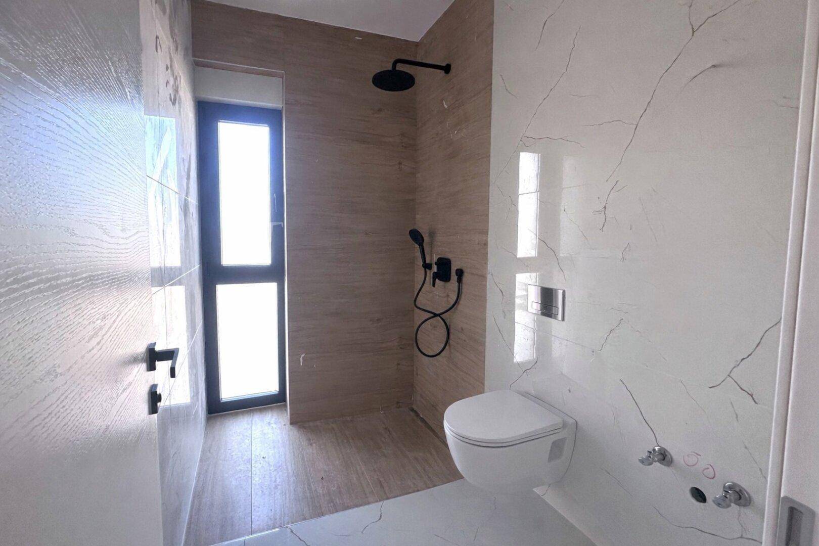 Modernes Badezimmer mit eleganten Marmorfliesen, Dusche und wandhängendem WC.