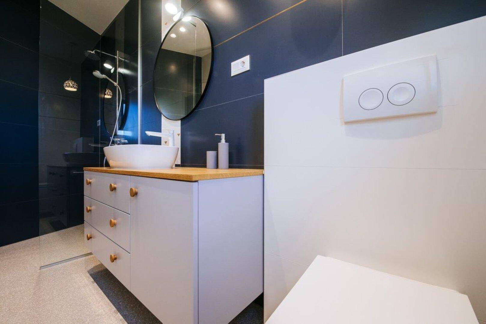 Elegantes Badezimmer mit dunklen Fliesen, modernem Waschtisch und integrierter Dusche.