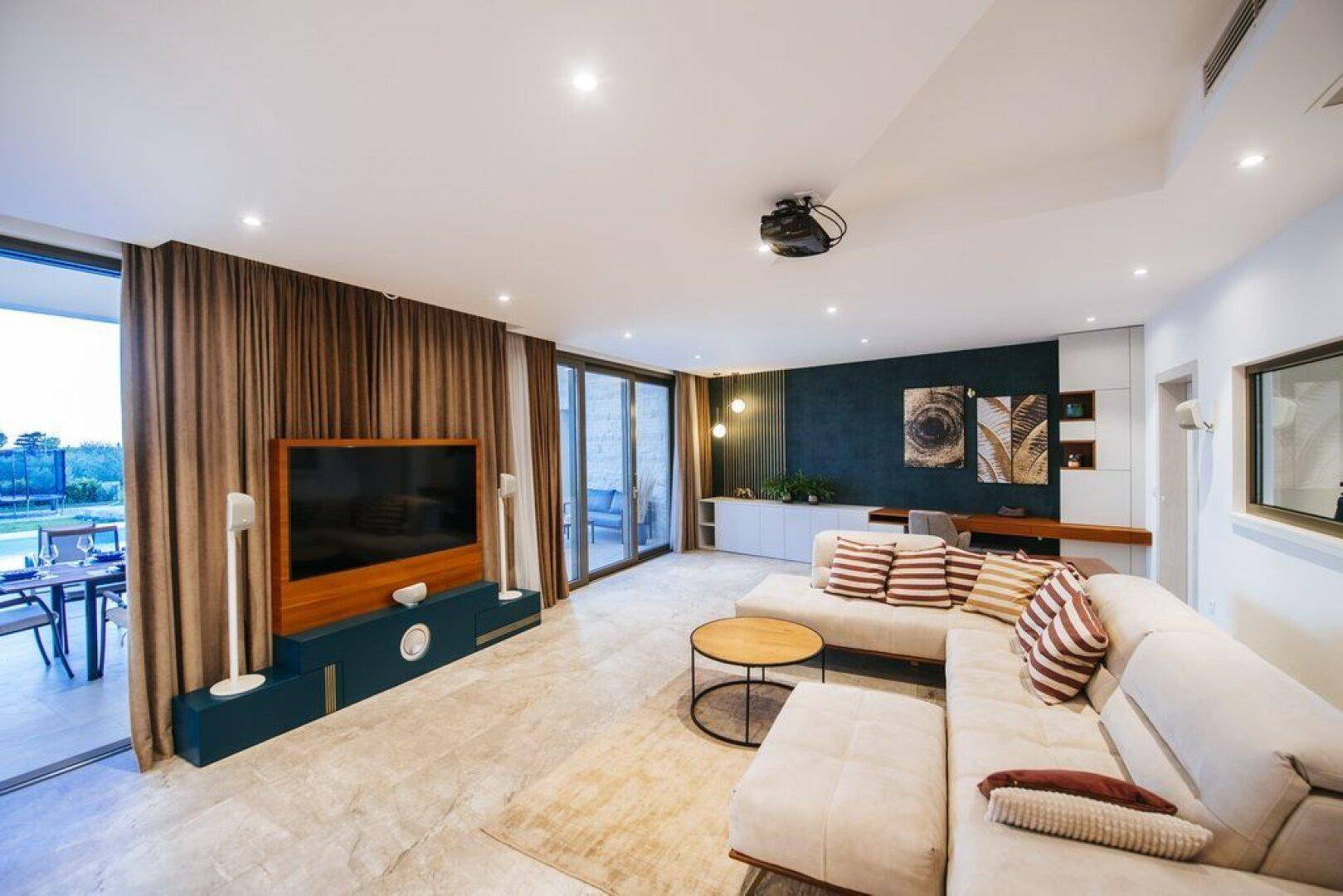 Geräumiges Wohnzimmer mit bequemer Couch, großem Fernseher und Zugang zur Terrasse.