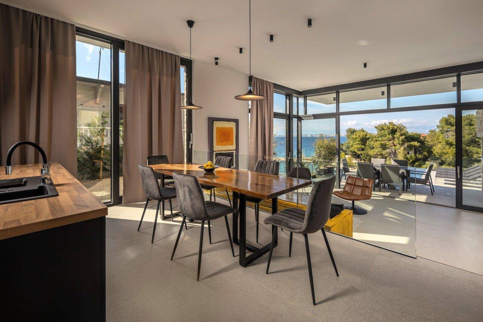 Heller Essbereich mit Holztisch, modernen Stühlen und großen Fenstern mit Meerblick.