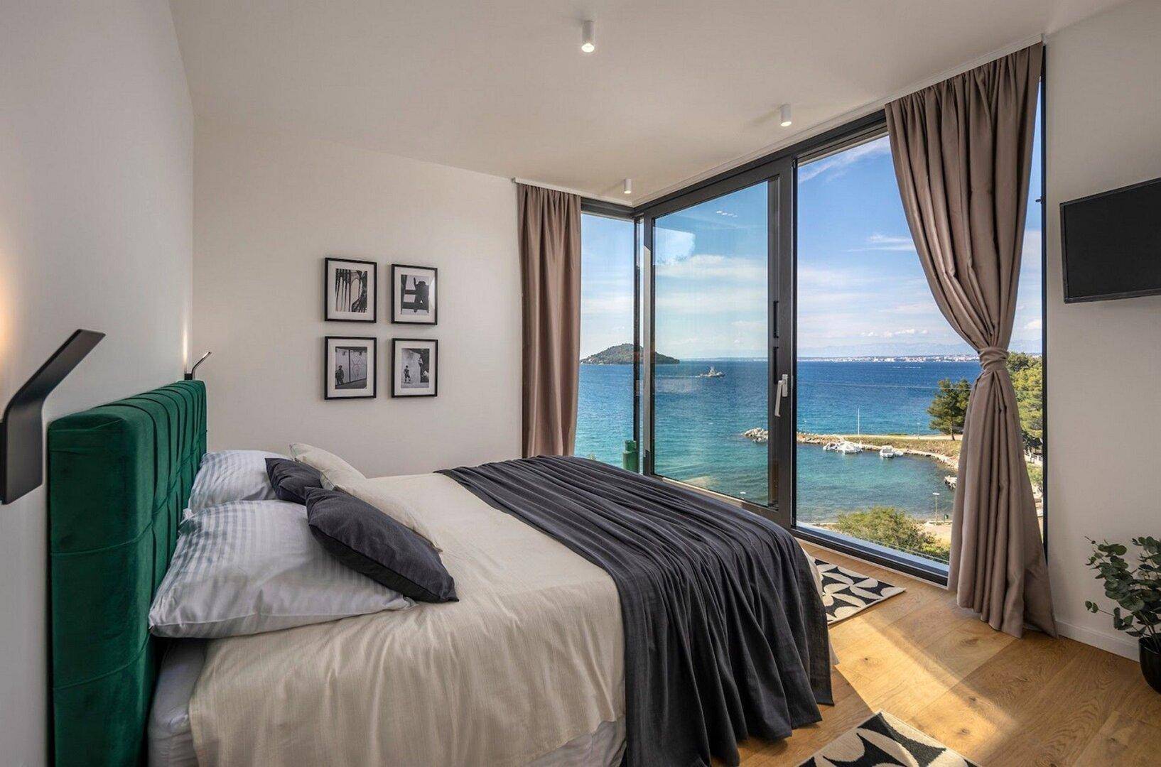 Schlafzimmer mit Holzboden, großem Bett und raumhohen Fenstern mit direktem Meerblick.