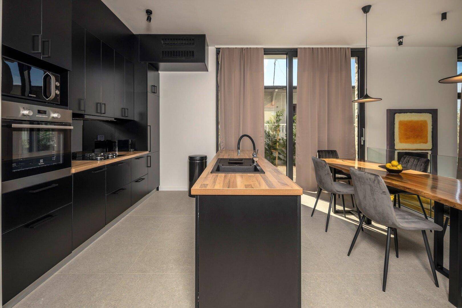 Moderne schwarze Küche mit Holz-Arbeitsplatten, integrierten Geräten und Essbereich.