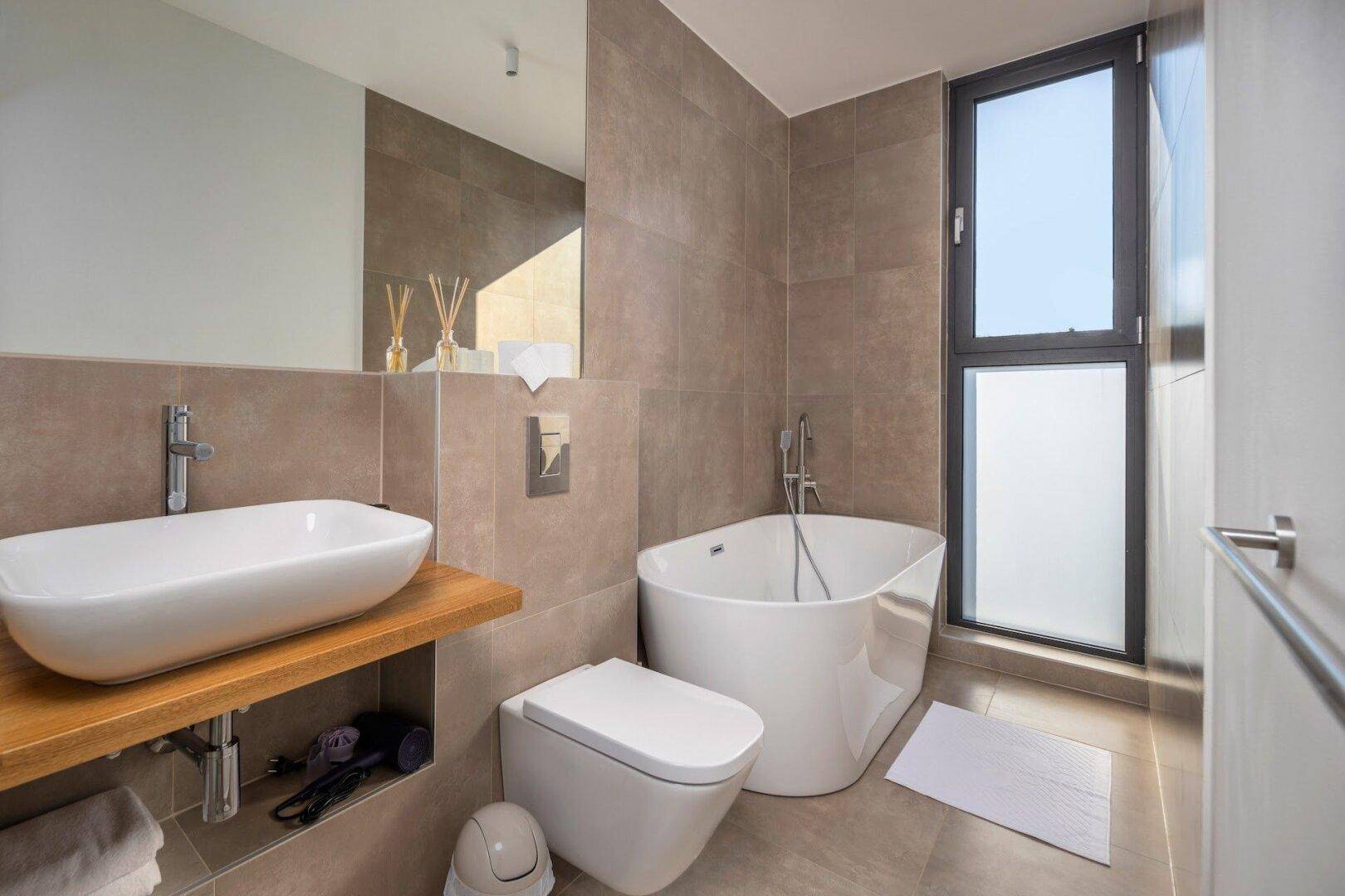 Elegantes Badezimmer mit freistehender Badewanne, Einzelwaschbecken und großem Fenster.