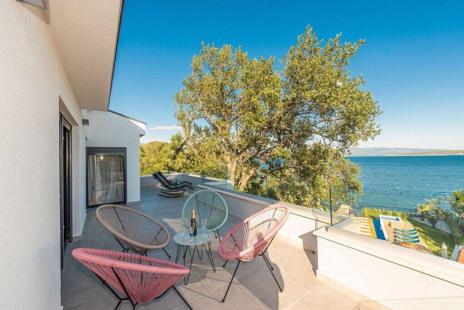 Sonniger Balkon mit bunten Sitzgelegenheiten und weitem Blick über das Meer und die Küste.