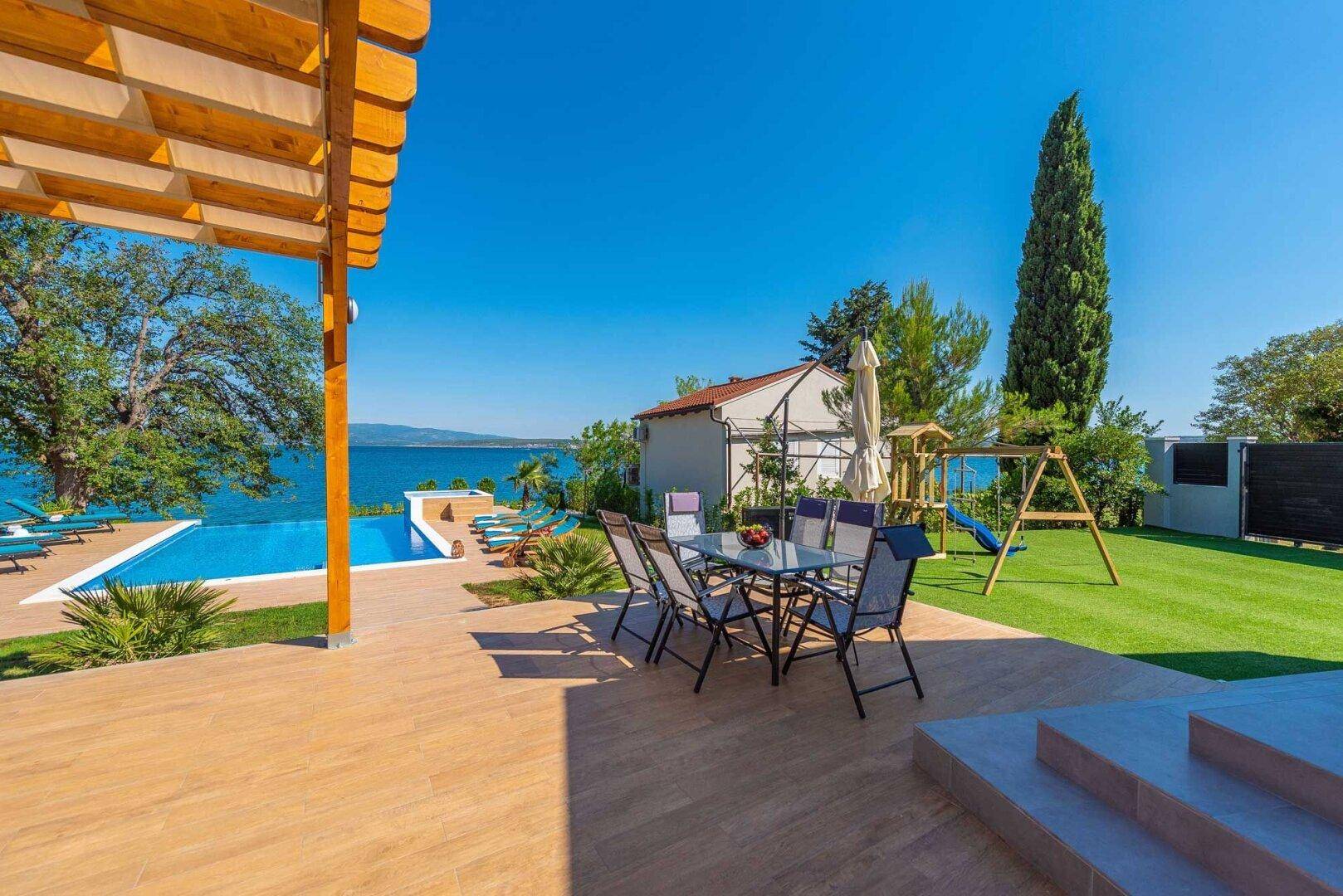Geräumige Terrasse mit Esstisch und Stühlen, umgeben von Grünflächen und Meerblick.