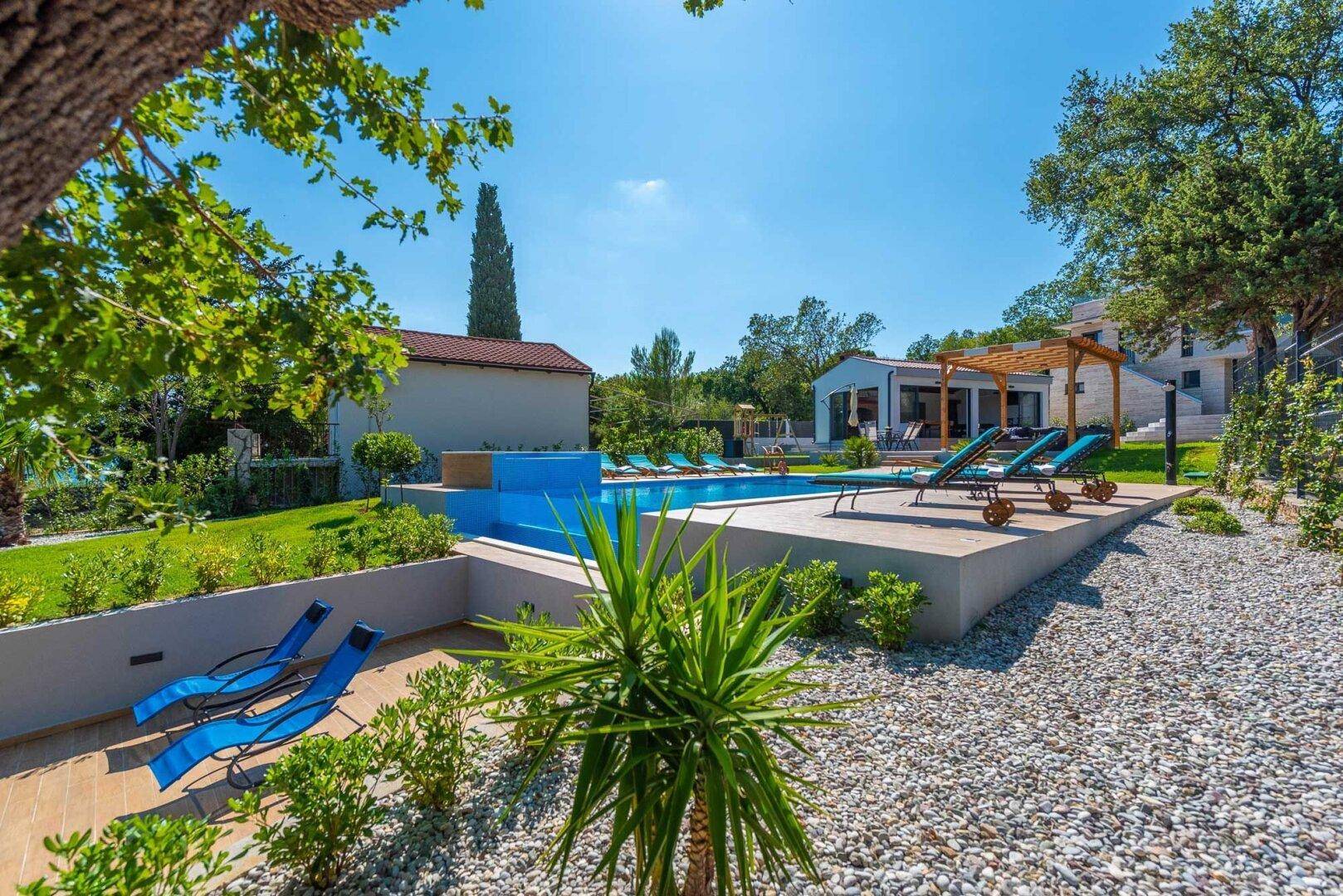Gepflegter Gartenbereich mit Kieswegen, Pflanzen und Blick auf den Pool und das Meer.